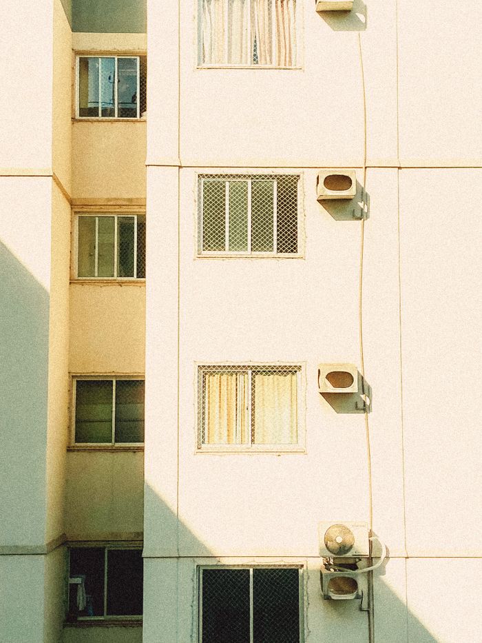 Bright sunlit exterior of an apartment building with window shadows, creating geometric patterns.